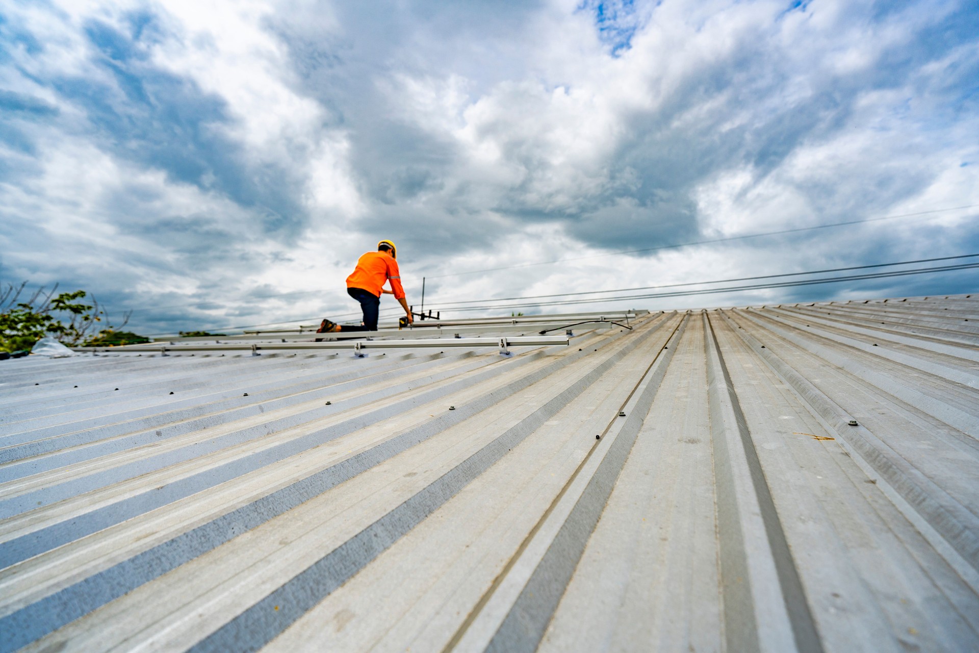 Technician in safety uniform and helmet kneeling on a rooftop, using a drill for precise installation work. A scene highlighting safety, professionalism, and technical expertise in construction.