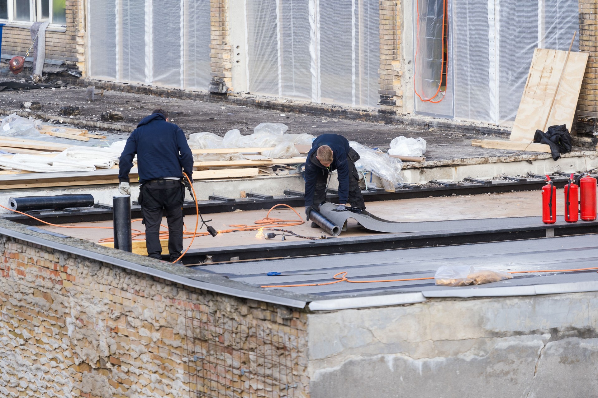 Workers installing waterproofing membrane and asphalt bitumen shingle on flat roof
